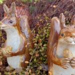 Zwei Eichhörnchen aus Keramik stehen im Garten und halten eine Haselnuss in ihren Händen