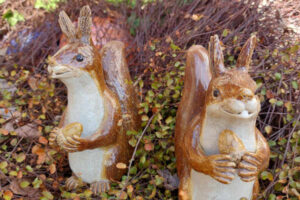 Zwei Eichhörnchen aus Keramik stehen im Garten und halten eine Haselnuss in ihren Händen